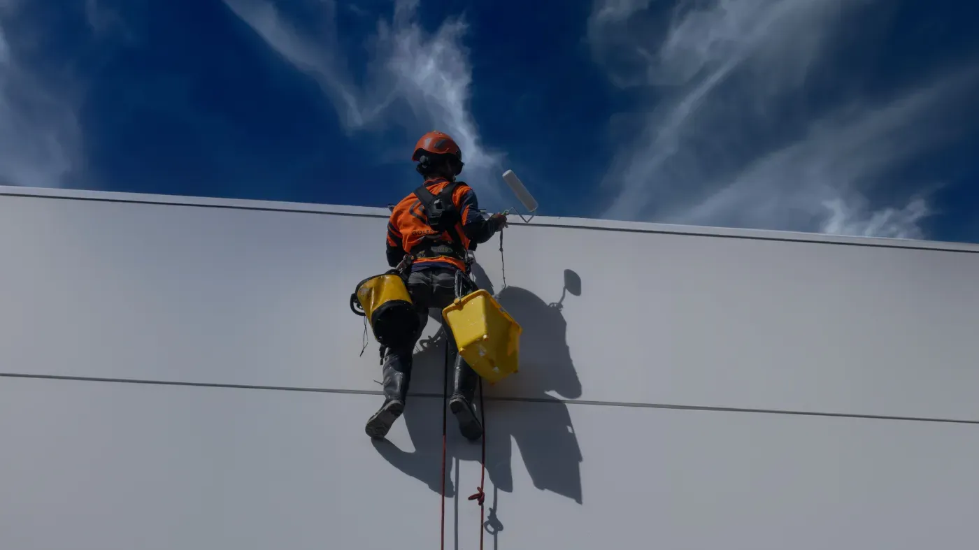 Pekerja melapisi dinding luar gedung bertingkat menggunakan tali akses