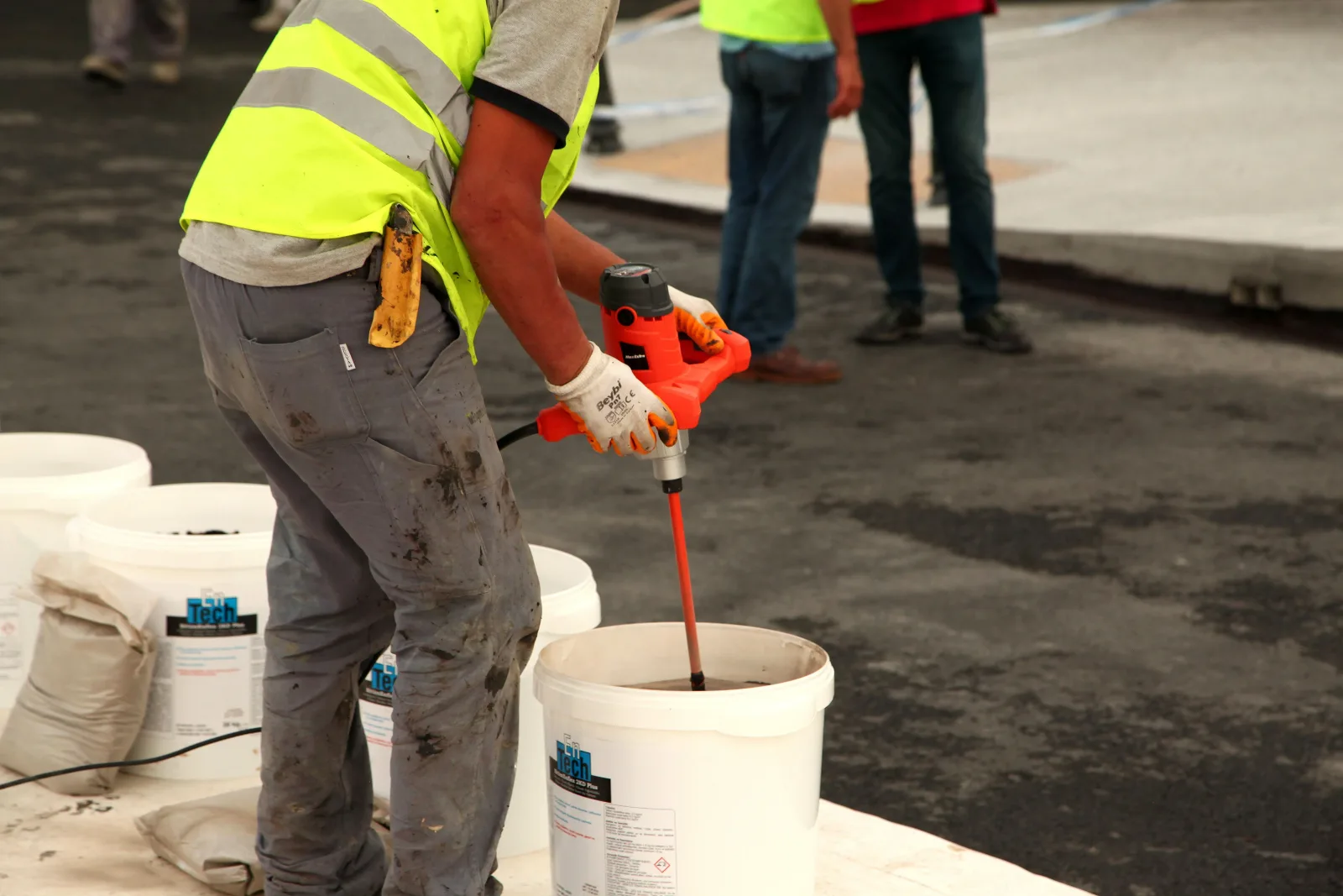 Pekerja mengaduk material coating dalam ember menggunakan mixer listrik sebelum diaplikasikan