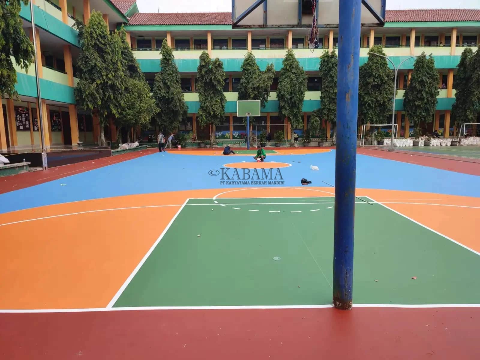 Lapangan basket dengan cat berwarna hijau, oranye, dan biru yang sedang dikerjakan