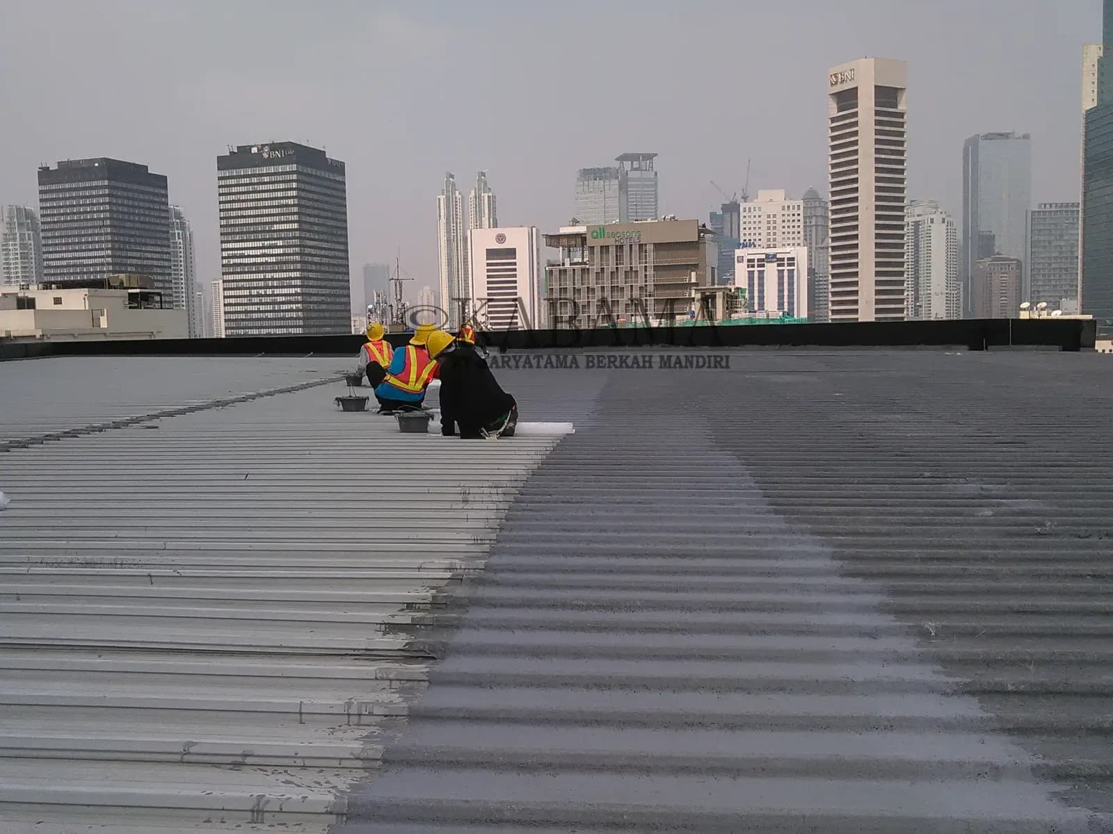 Tiga pekerja melapisi atap metal gedung bertingkat dengan lapisan anti air
